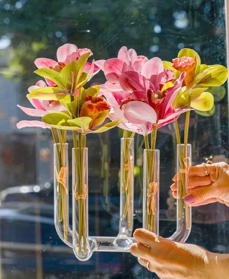 Mãos segurando vaso de vidro de cinco pontas com flores
